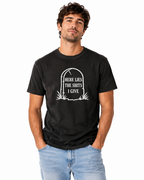 A man wearing a black graphic t-shirt with a white tombstone design that reads 'HERE LIES THE SHITS I GIVE paired with light blue jeans, against a plain white background.