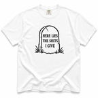 A white short-sleeve crewneck t-shirt with a black graphic of a tombstone on the chest containing the text 'HERE LIES THE SHITS I GIVE'.