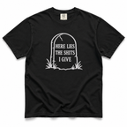 A black short-sleeve crewneck t-shirt with a white graphic of a tombstone that reads 'HERE LIES THE SHITS I GIVE' on a plain white background.