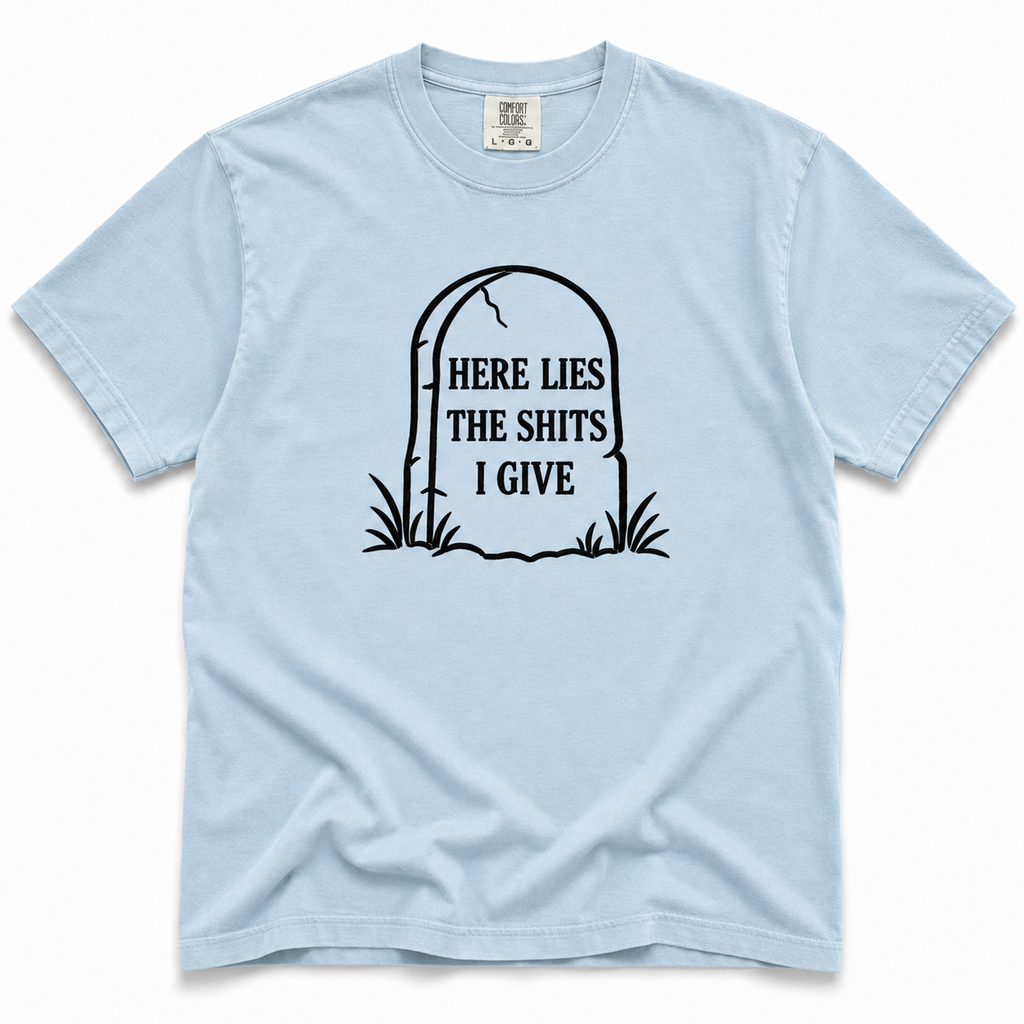 Chambray crewneck T-shirt with a black tombstone graphic reading “HERE LIES THE SHITS I GIVE,” displayed flat against a white background.