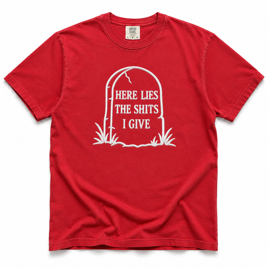 A red short-sleeve crewneck t-shirt with a white graphic of a tombstone on the chest containing the text 'HERE LIES THE SHITS I GIVE'.