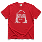 A red short-sleeve crewneck t-shirt with a white graphic of a tombstone on the chest containing the text 'HERE LIES THE SHITS I GIVE'.