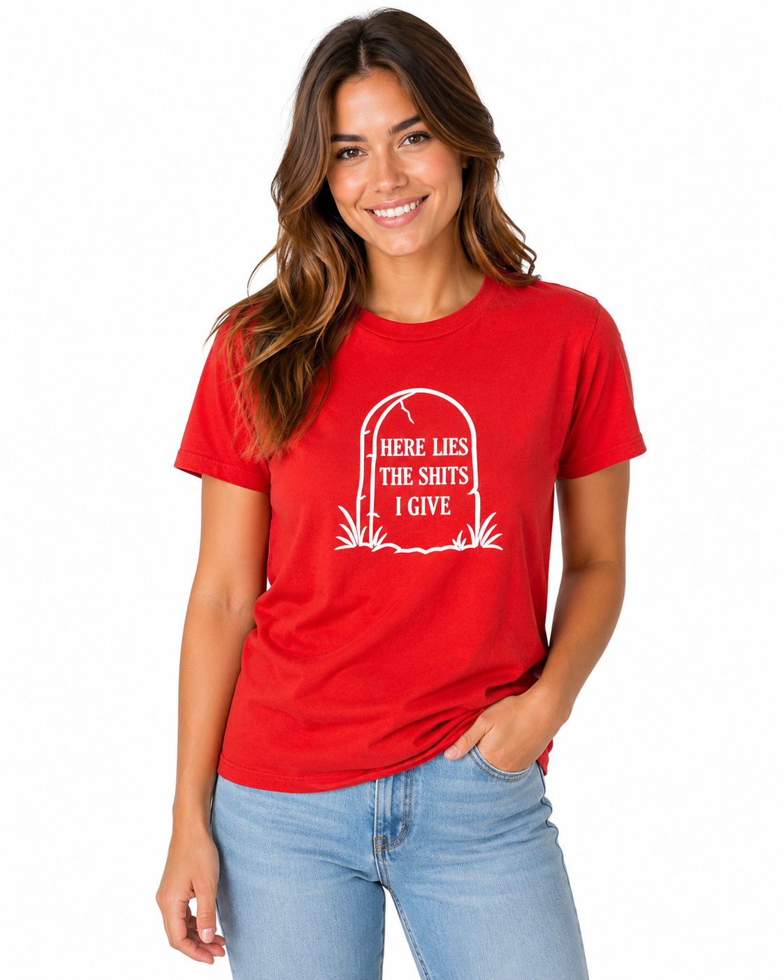 A woman wearing a bright red short-sleeve t-shirt with a white tombstone graphic and the text 'HERE LIES THE SHITS I GIVE paired with light blue jeans, against a plain white background.