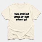ivory crewneck t-shirt with the text 'I'm on some shit Jehovah ain't even witness yet' printed in black sans-serif font across the chest, displayed on a light gray background.