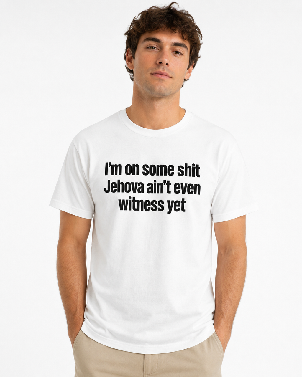 A man wearing a white crewneck t-shirt with the black printed text 'I'm on some shit Jehovah ain't even witness yet', paired with khaki pants, against a plain white background.