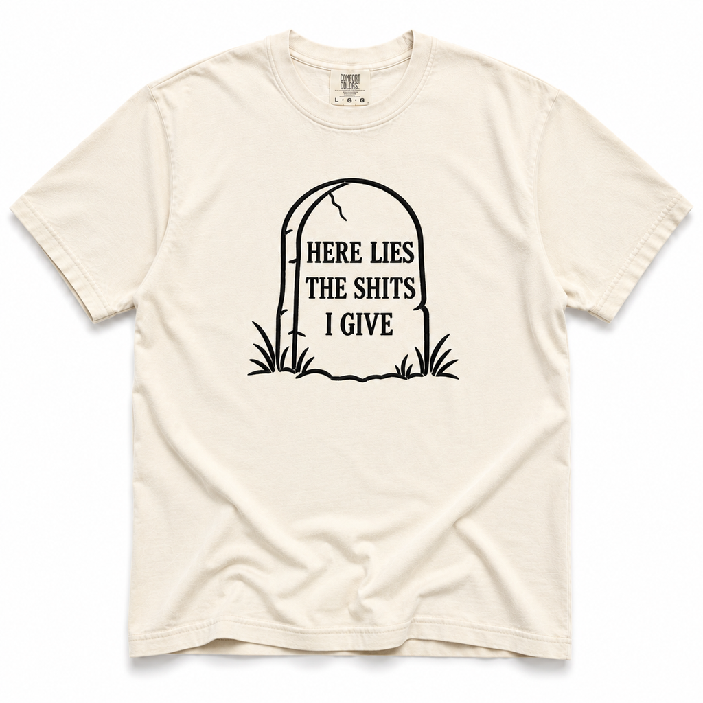 ivory crewneck t-shirt with a black graphic of a tombstone that reads 'HERE LIES THE SHITS I GIVE' on a plain white background.