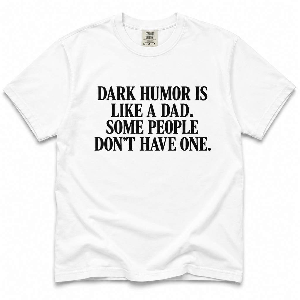 A white short-sleeve crewneck t-shirt with bold black text on the front reading 'DARK HUMOR IS LIKE A DAD. SOME PEOPLE DON'T HAVE ONE.