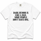 A white short-sleeve crewneck t-shirt with bold black text on the front reading 'DARK HUMOR IS LIKE A DAD. SOME PEOPLE DON'T HAVE ONE.