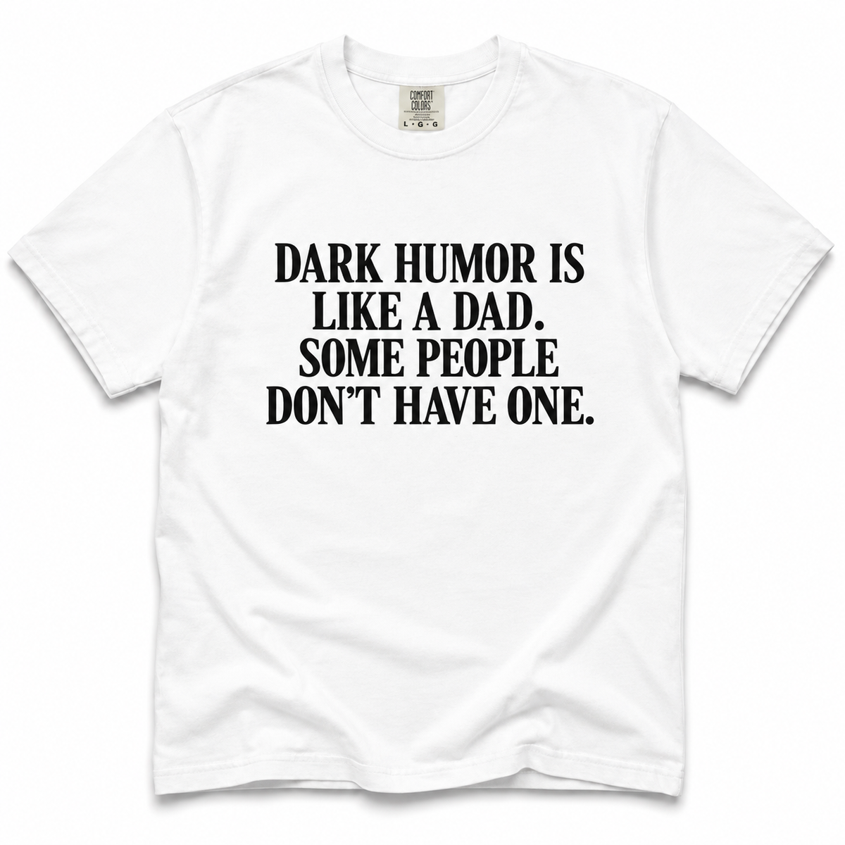 A white short-sleeve crewneck t-shirt with bold black text on the front reading 'DARK HUMOR IS LIKE A DAD. SOME PEOPLE DON'T HAVE ONE.