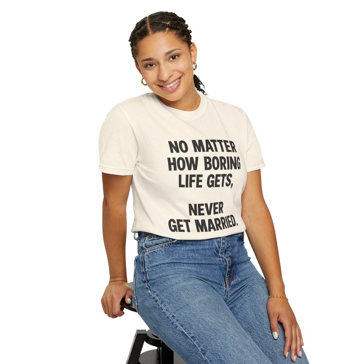 Woman wearing an Ivory graphic T-shirt with bold black “No Matter How Boring Life Gets, Never Get Married” text, paired with blue jeans against a white background.