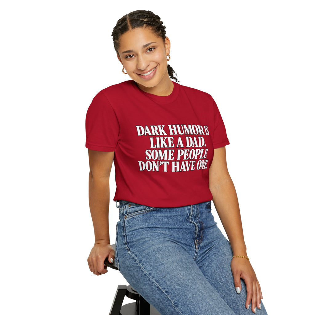 A woman wearing a red graphic t-shirt with white text that reads 'DARK HUMORS LIKE A DAD. SOME PEOPLE DON'T HAVE ONE.